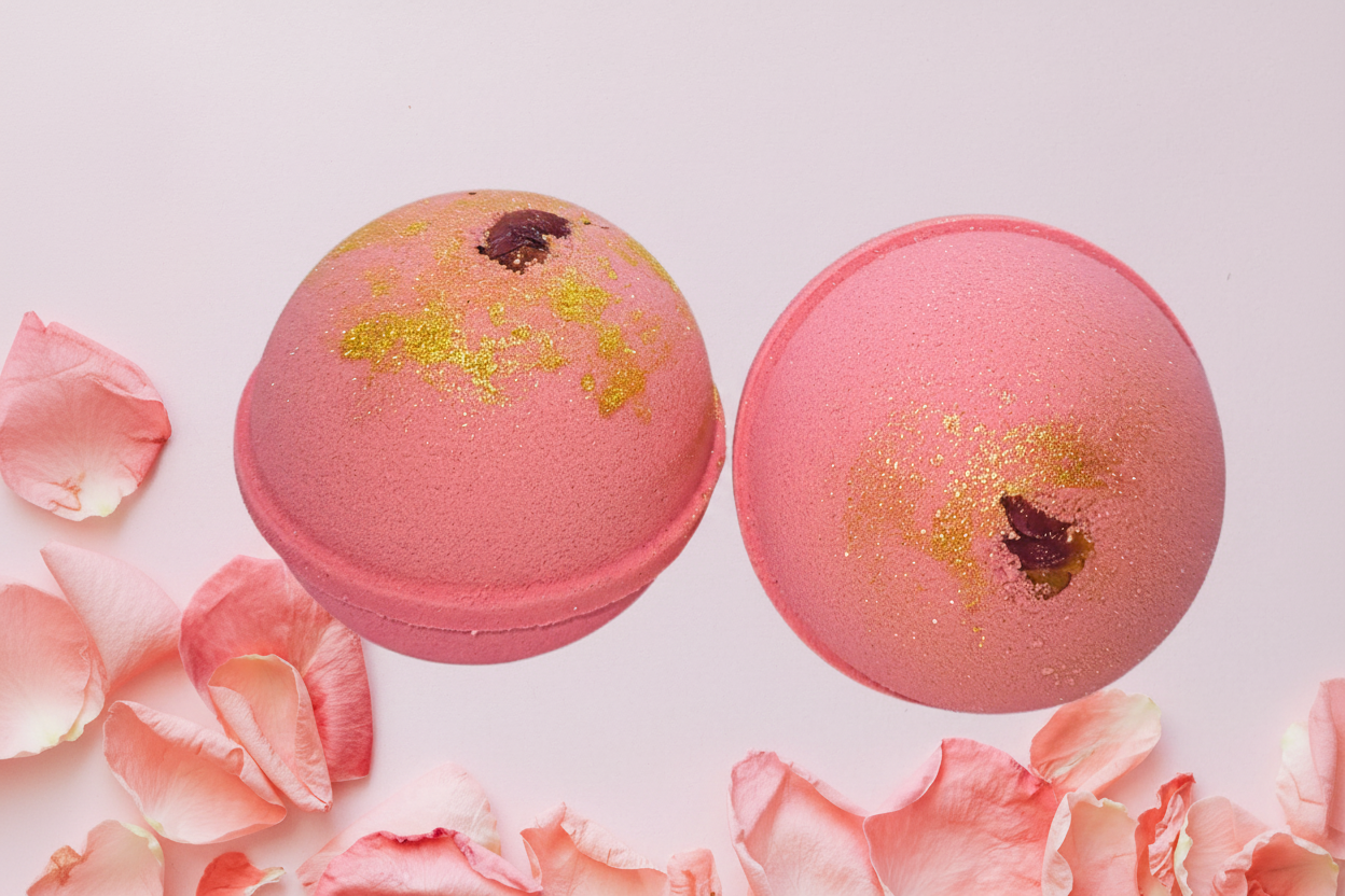 Two pink bath bombs with gold glitter and rose petals on a white background.