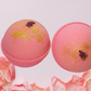 Two pink bath bombs with gold glitter and rose petals on a white background.