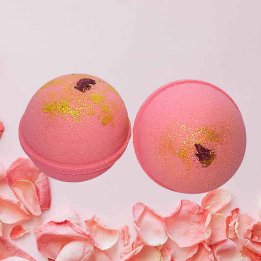 Two pink bath bombs with gold glitter and rose petals on a white background.